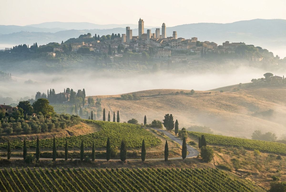Medieval towers of San Gimignano above vineyards and misty rolling Tuscan hills at sunrise