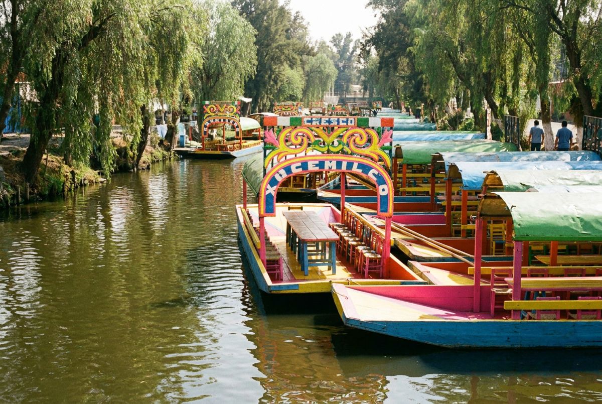 Colorful painted trajinera boats lined up on a tree-shaded canal in Xochimilco, Mexico City