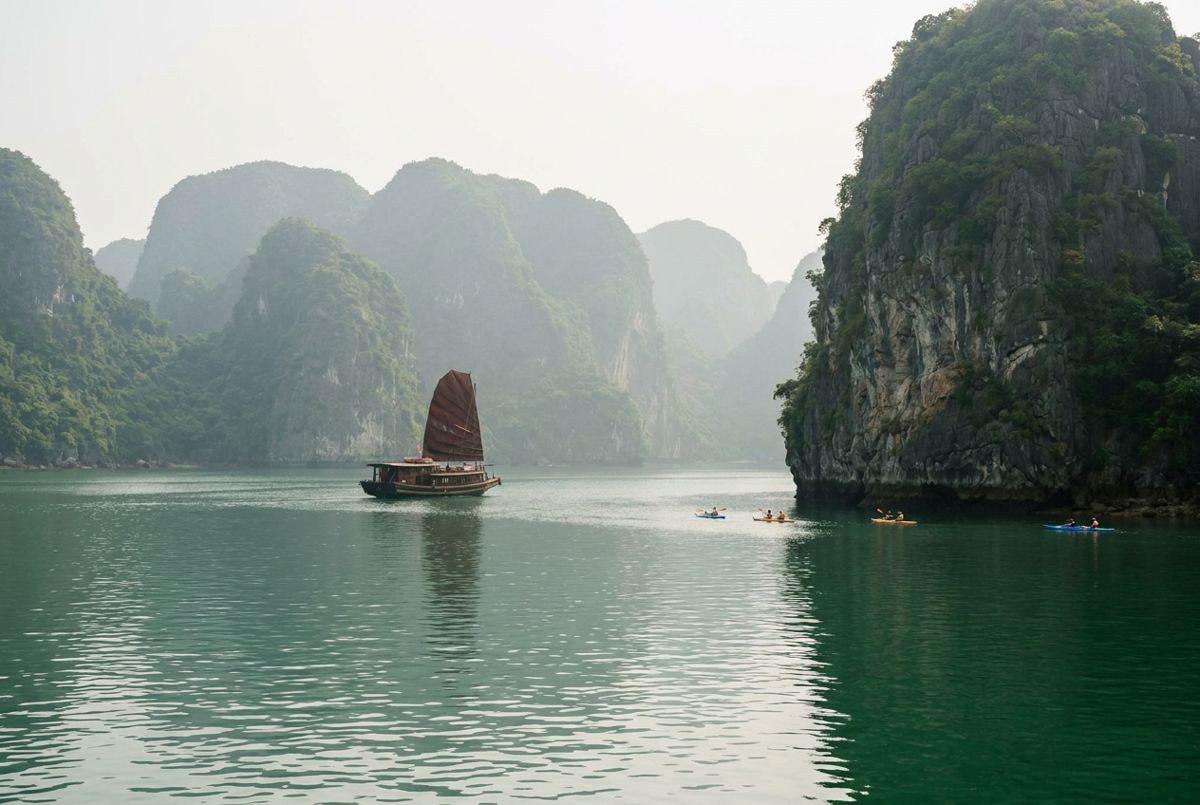 Limestone karst islands and a wooden junk boat on the emerald waters of Ha Long Bay in morning haze
