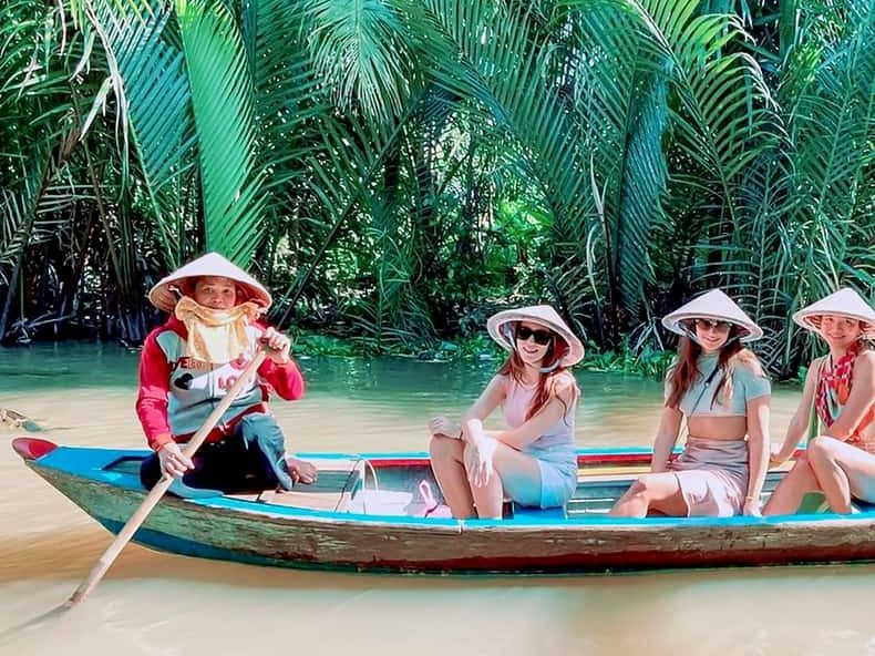Tourists in conical hats paddling a sampan through palm-lined waterways