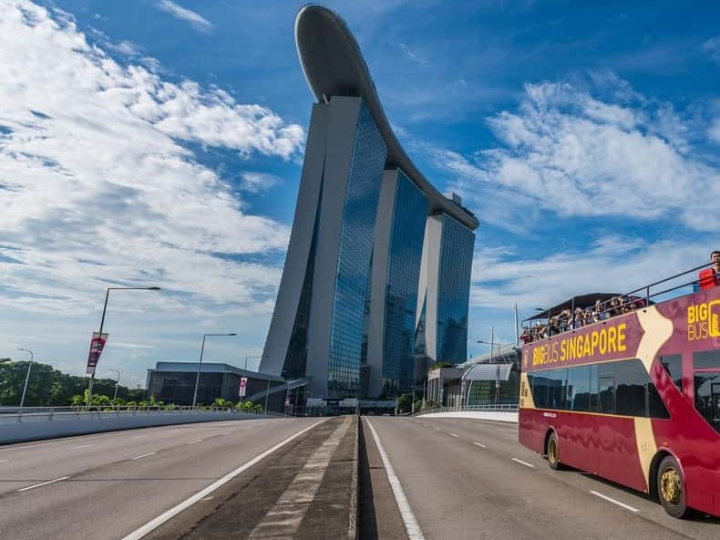 A red open-top bus driving toward Marina Bay Sands