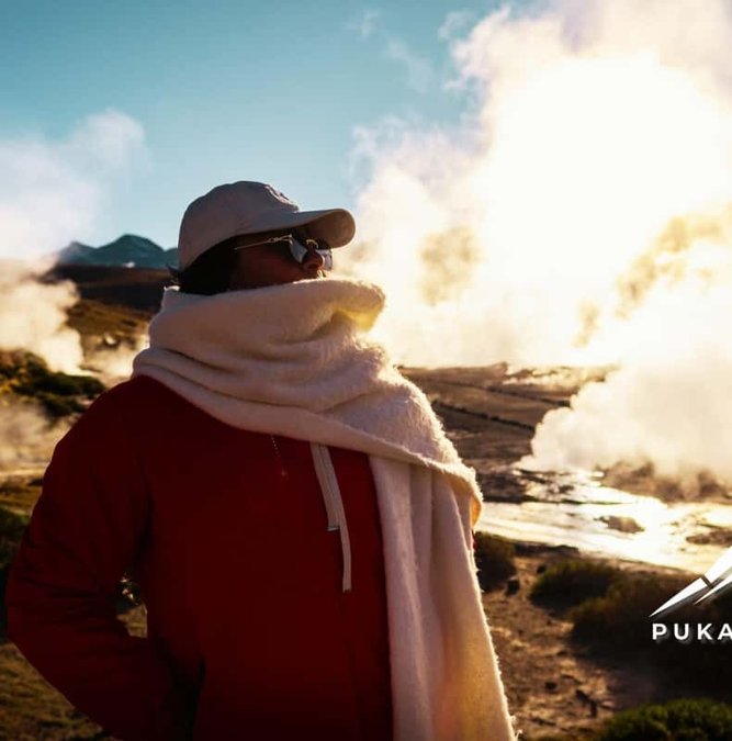Traveler in a shawl beside steaming Tatio geysers at sunrise