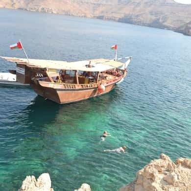 Omani dhow anchored in a Musandam fjord with a swimmer below