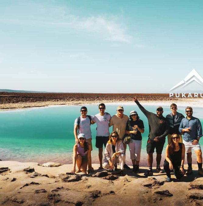 Travelers beside a turquoise salt lagoon at Baltinache