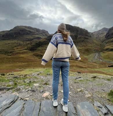Hiker standing on rocks facing the mountains of Glencoe
