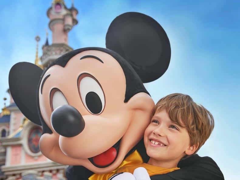 Mickey Mouse hugging a smiling child in front of the Disneyland Paris castle