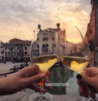 Two glasses of white wine raised against a Venice canal at sunset
