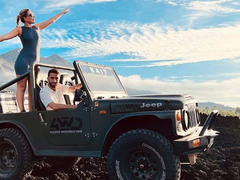 A woman standing in an open jeep on the black lava field of Mount Batur