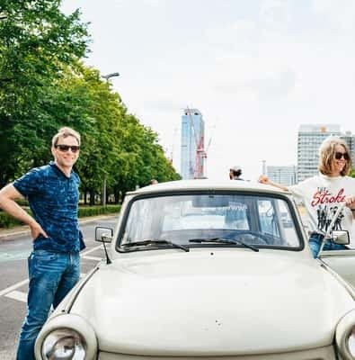 A couple leaning on a white Trabant car on a Berlin street