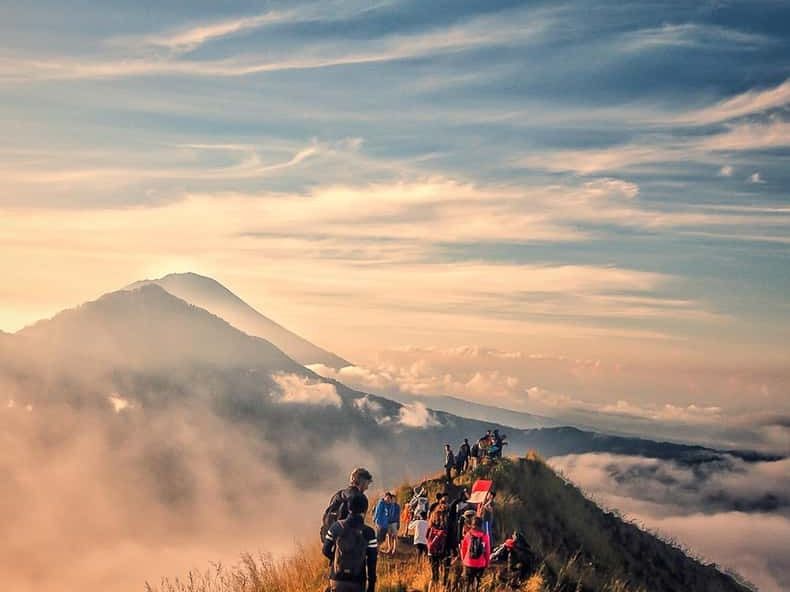 Hikers on the ridge of Mount Batur at sunrise with clouds below