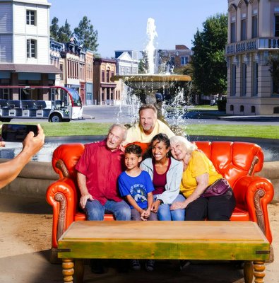 Six people on the iconic orange couch from Friends, posing for a photo in front of a fountain.