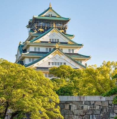 Osaka Castle exterior with lush green trees and blue sky.