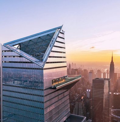 Visitors on Edge Observation Deck with New York City skyline at sunset.