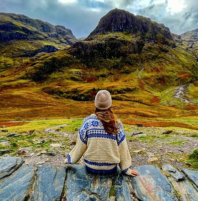 Person sitting on rocks overlooking the Highlands landscape near Loch Ness on an Edinburgh day trip.