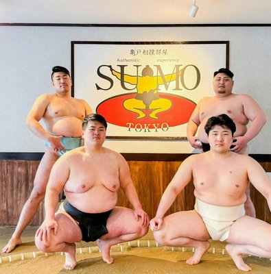 Sumo wrestlers posing in front of a Tokyo sign at an authentic sumo experience.