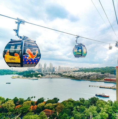 Cable car with Pokémon theme over Sentosa, Singapore, with city skyline and water view.