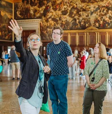 Guide leading a tour group inside Doge's Palace, Venice, with historic paintings in the background.