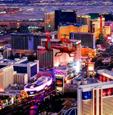 Aerial view of the illuminated Las Vegas Strip at night with a helicopter in the foreground.