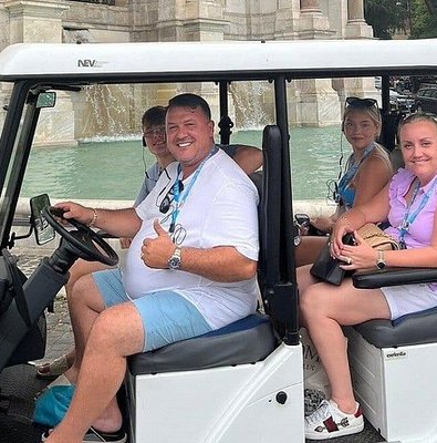 Visitors riding an electric golf cart past the Trevi Fountain