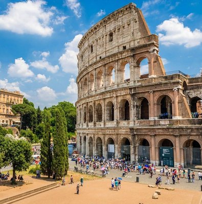 The Colosseum under a blue sky with visitors in the square