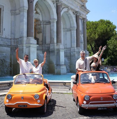 Two vintage Fiat 500s with passengers in front of a Roman fountain
